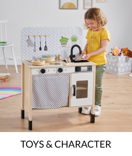 A girl wearing green trousers and a yellow top playing with a wooden kitchen counter toy.