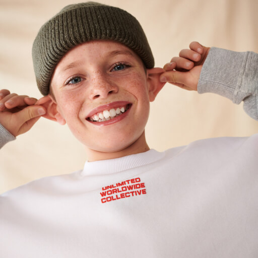 Child wearing white slogan jumper and khaki beanie.