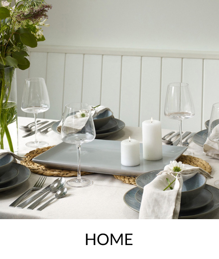 A dinner table topped with wine glasses, silver cutlery, grey crockery, candles and a vase of flowers.